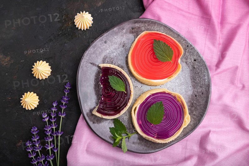 Sweet tartlets with jelly and milk cream with cup of coffee on a black concrete background and pink textile. top view, flat lay, close up
