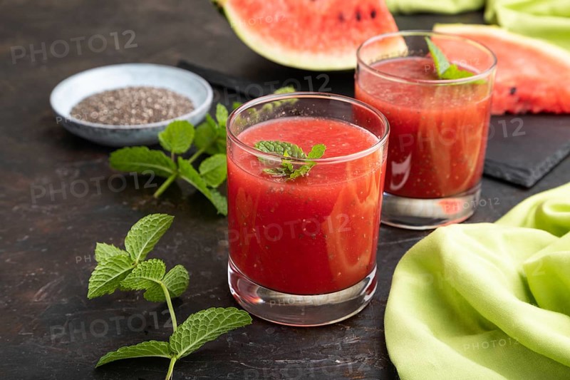 Watermelon juice with chia seeds and mint in glass on a black concrete background with green textile. Healthy drink concept. Side view, close up