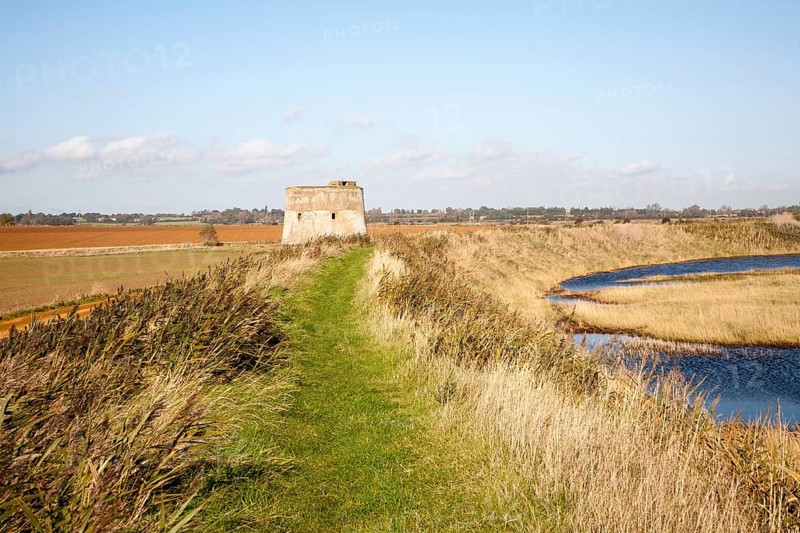 Coastal flood defence dyke passing historic martello tower Z, Alderton, Suffolk, England, UK