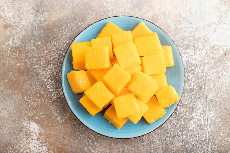 Dried and candied mango cubes on blue plate on brown concrete background. Top view, flat lay, close up, vegan, vegetarian food concept