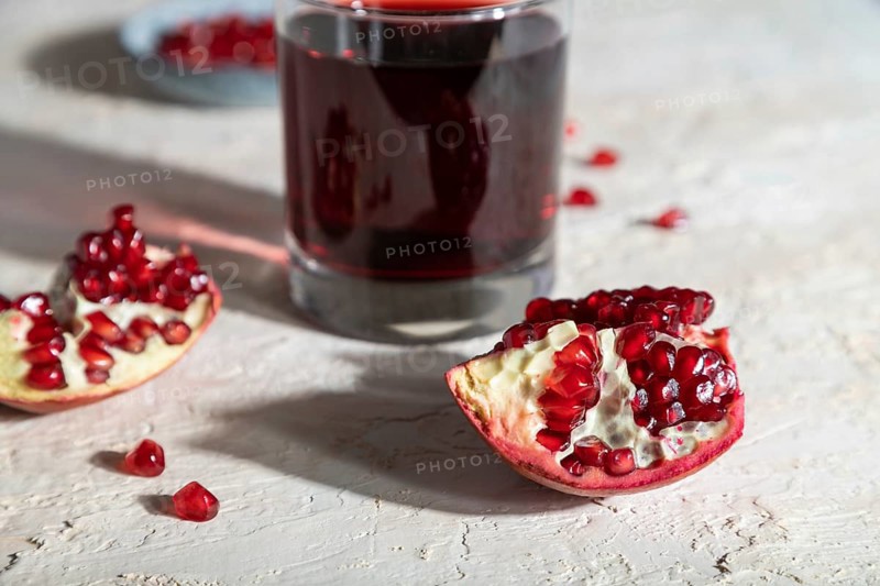 Glass of pomegranate juice on a white concrete background. Hard light, contrast. Side view, close up, selective focus
