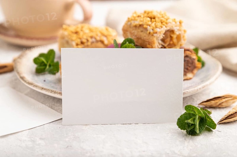 White paper business card and set of eclair on gray concrete background. side view, close up, selective focus, still life. Breakfast, morning, concept