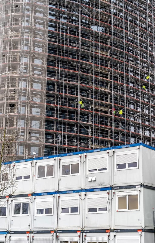 Large construction site, construction of a high-rise residential building, scaffolded shell, already fitted with windows, in front of it containers for offices, accommodation, washrooms, storage, for the construction workers