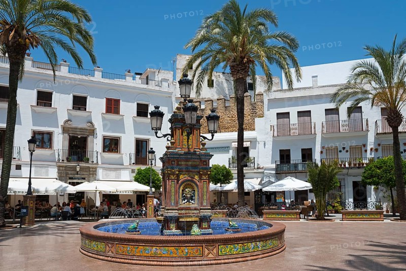 A central fountain in a sunny plaza surrounded by white buildings and palm trees, fountain with azulejos, Plaza de España, square, old town, Vejer de la Frontera, Cadiz province, Cadiz, Andalusia, Spain, Europe