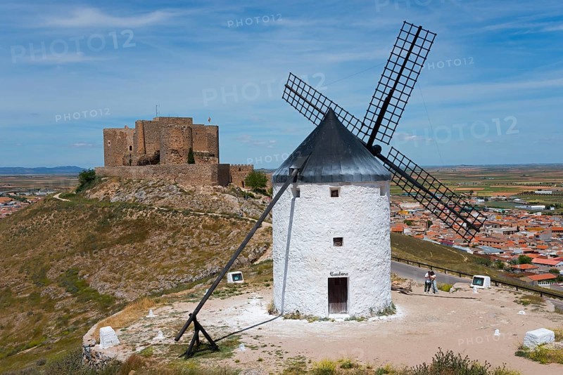 An old windmill in front of a medieval castle on a hill with a village in the background under a blue sky, Consuegra, Toledo, Castilla-La Mancha, Route of Don Quixote, Spain, Europe