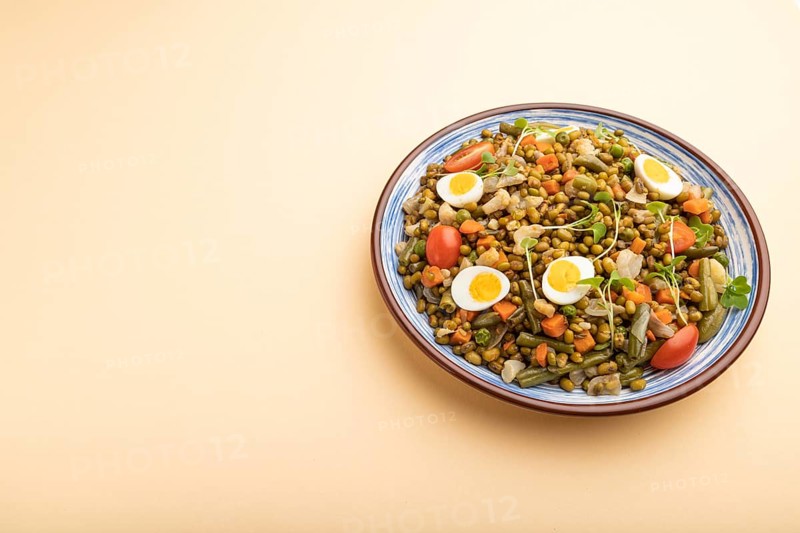 Mung bean porridge with quail eggs, tomatoes and microgreen sprouts on a pastel orange background. Side view, copy space, close up
