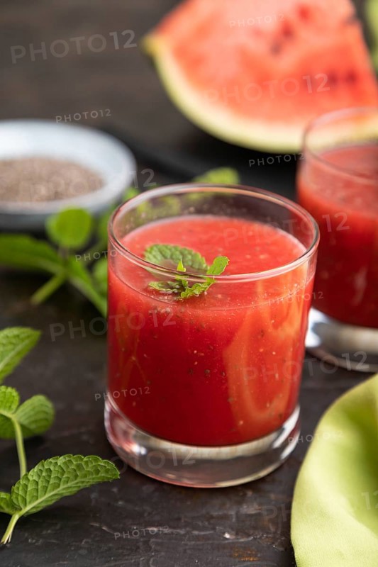Watermelon juice with chia seeds and mint in glass on a black concrete background with green textile. Healthy drink concept. Side view, close up, selective focus