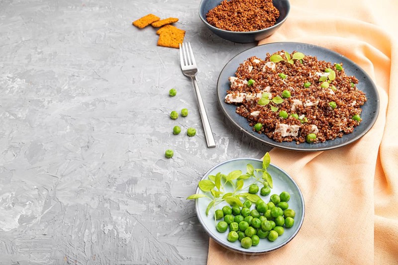 Quinoa porridge with green pea and chicken on ceramic plate on a gray concrete background and orange textile. Side view, close up, copy space
