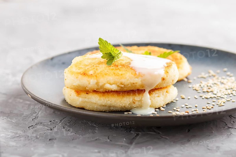 Cheese pancakes on a blue ceramic plate with milk sauce on a gray concrete background. side view, close up, selective focus