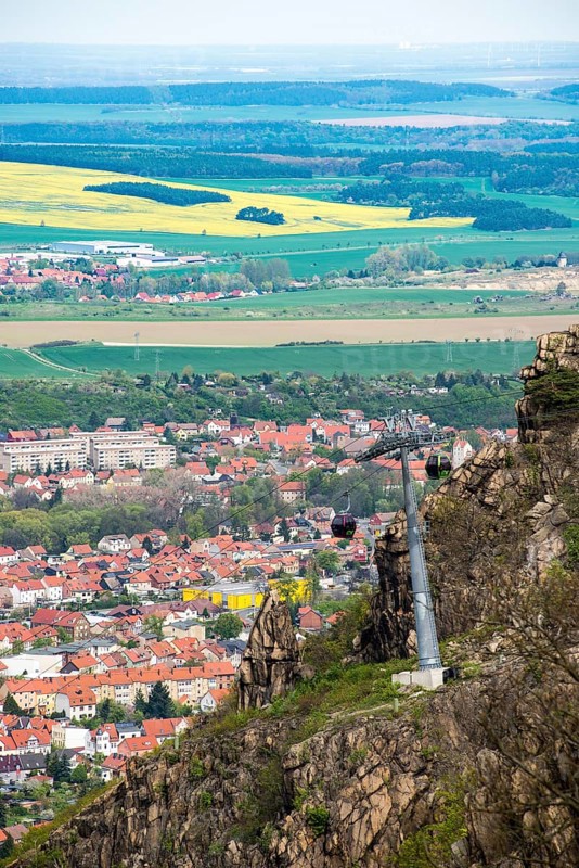View from the Hexentanzplatz to the cable car, the town of Thale and the Harz foreland with fields and forests, rape blossom, cable car or gondola lift over a steep mountain slope with cabins or gondolas and cable car supports or stands or girders, spring, springtime, Erlebniswelt Thale, Saxony-Anhalt, Germany Saxony-Anhalt, Germany, Europe