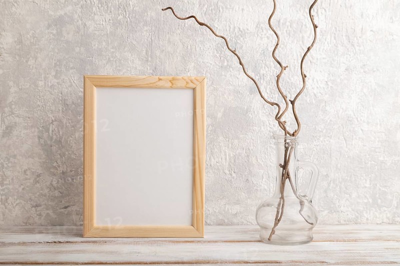 White wooden frame mockup with dried wine branch in glass on gray concrete background. Blank, vertical orientation, still life, copy space
