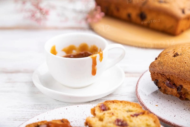 Homemade cake with raisins, almonds, soft caramel and a cup of coffee on a white wooden background. Side view, close up, selective focus