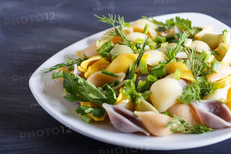 Conchiglie colored pasta with fresh greengrocery on black wooden background. close up, selective focus