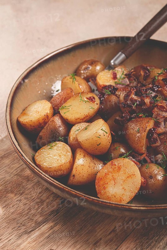 A bowl of perfectly roasted potatoes is served with caramelized onions and sprinkled with fresh herbs, highlighting a warm and inviting meal setting.