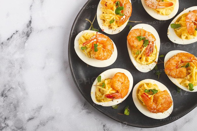 Boiled eggs stuffed with yolk and seasoned with mayonnaise, stuffed eggs with shrimp, on a black plate, selective focus, close-up, no people