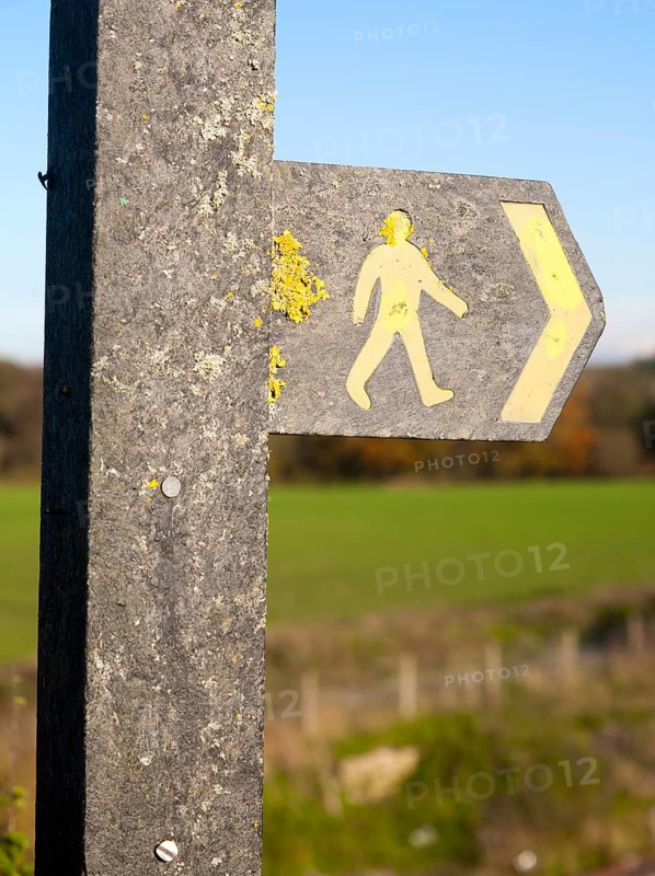 Close up of footpath sign with yellow human figure walking and direction arrow pointing the way, Wiltshire, England, UK