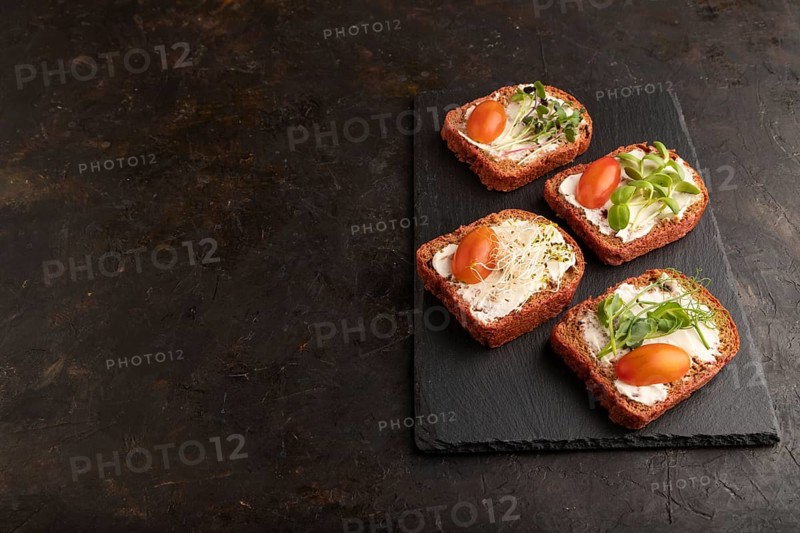 Red beet bread sandwiches with cream cheese, tomatoes and microgreen on black concrete background. Side view, copy space