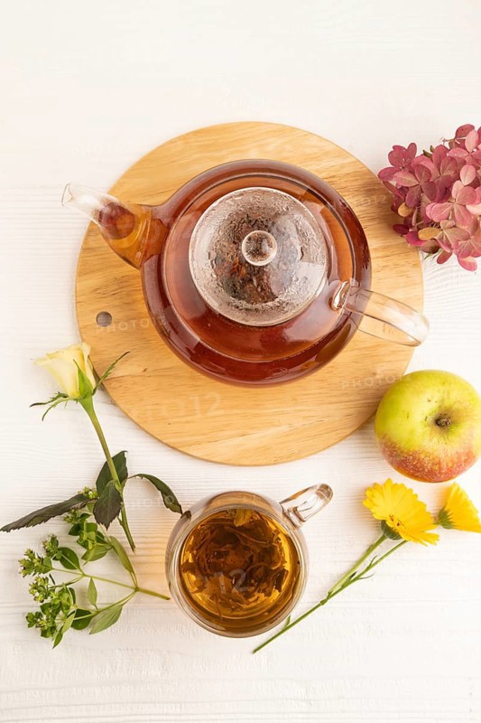 Red tea with herbs in glass teapot on white wooden background. Healthy drink concept. Top view, flat lay, close up