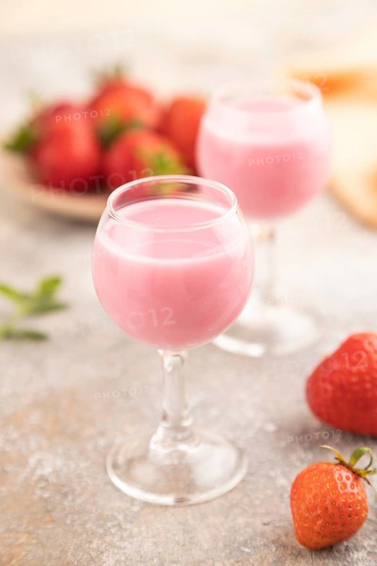 Sweet strawberry liqueur in glass on a gray concrete background and orange textile. side view, close up, selective focus