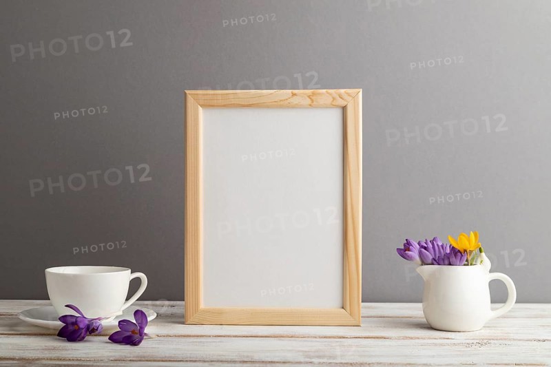Beige wooden frame mockup with snowdrop crocus flowers and white coffee cup on gray paper background. Blank, vertical orientation, still life, copy space