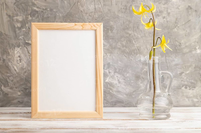 Wooden frame with yellow trout lily or dogtooth violet flowers in glass on gray concrete background. side view, copy space, mockup, template, spring, summer minimalism concept