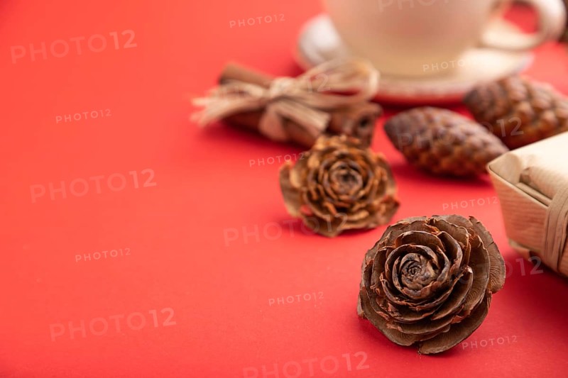 Christmas or New Year composition. Decorations, box, cinnamon, cones, fir and spruce branches, cup of coffee, on a red paper background. Side view, copy space