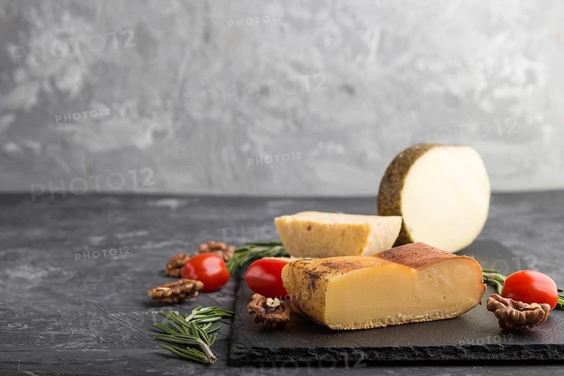 Smoked cheese and various types of cheese with rosemary and tomatoes on black slate board on a black concrete background. Side view, copy space, selective focus