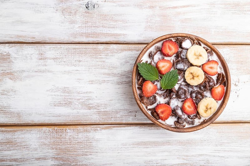 Chocolate cornflakes with milk and strawberry in wooden bowl on white wooden background. Top view, flat lay, copy space