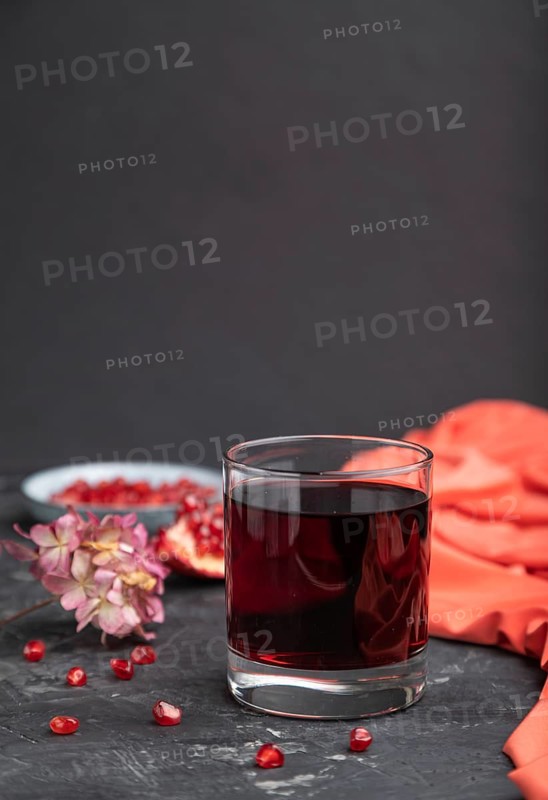 Glass of pomegranate juice on a black concrete background with red textile. Side view, close up, copy space