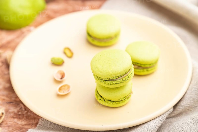 Green macarons or macaroons cakes with cup of coffee on a brown concrete background and linen textile. Side view, close up, selective focus