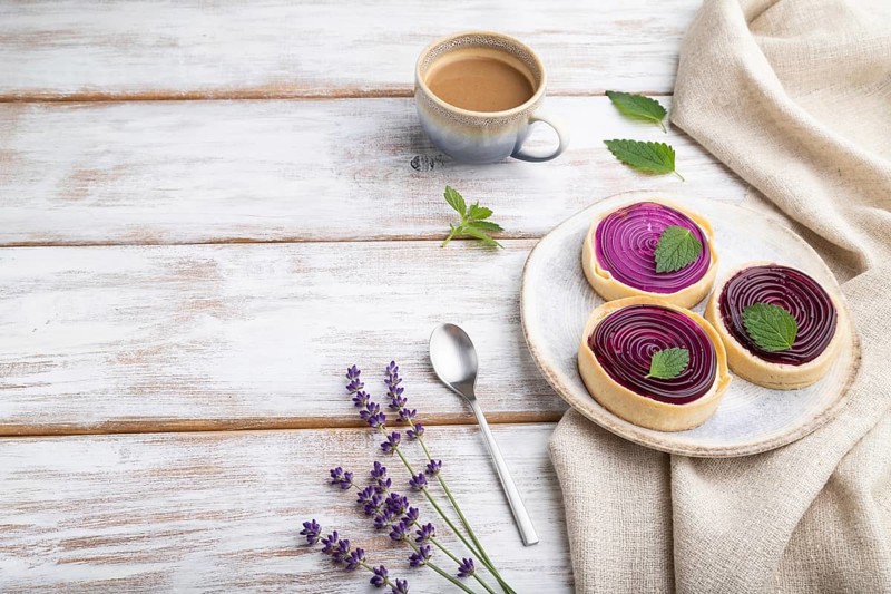 Sweet tartlets with jelly and milk cream with cup of coffee on a white wooden background and linen textile. Side view, copy space
