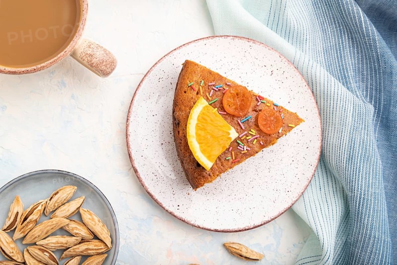 Orange cake with almonds and a cup of coffee on a white concrete background and blue linen textile. Top view, flat lay, close up