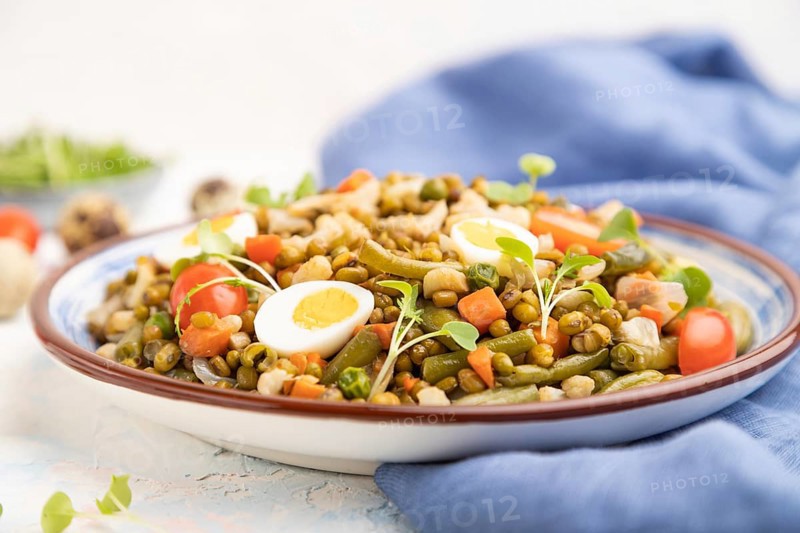 Mung bean porridge with quail eggs, tomatoes and microgreen sprouts on a white concrete background and blue textile. Side view, close up, selective focus