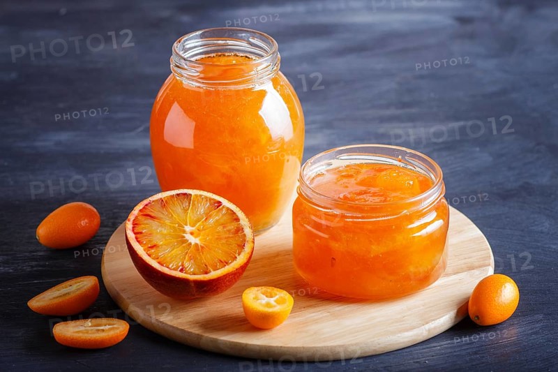 Orange and kumquat jam in a glass jar with fresh fruits on black wooden background. Homemade, close up