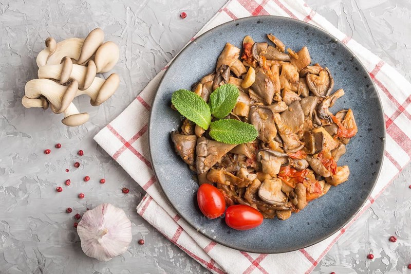 Fried oyster mushrooms with tomatoes on gray concrete background. Top view, close up