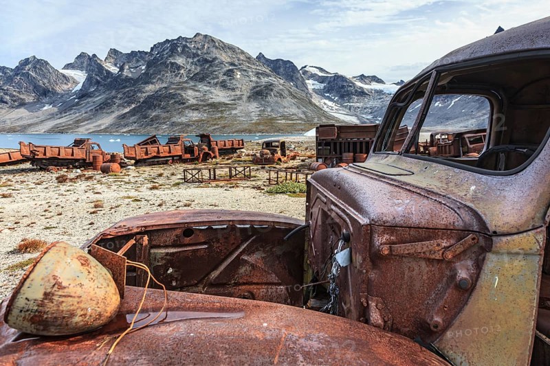 Rusted car and oil drums in front of steep mountains, remains of a US airbase from the Second World War, Ikateq Fjord, East Greenland, Greenland, North America