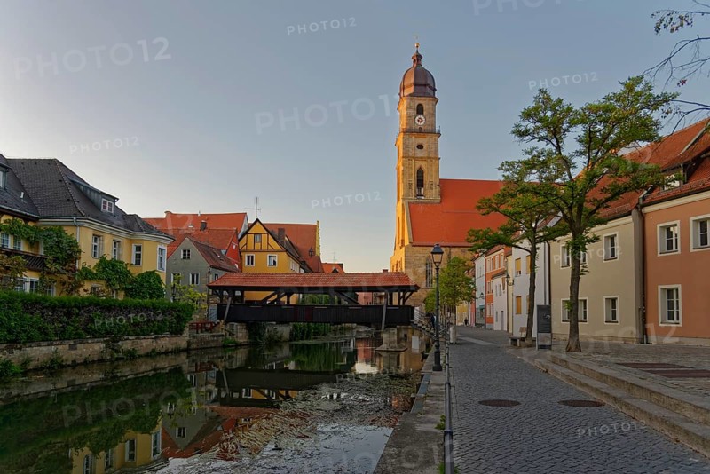 The setting sun bathes everything in warm light and reflects the Basilica of St Martin and the historic ship bridge in the River Vils, Amberg, Upper Palatinate, Bavaria, Germany, Europe