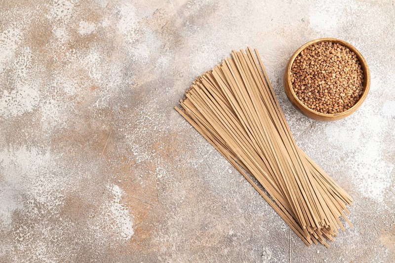 Japanese buckwheat soba noodles with tomato, eggs, spices, herbs on brown concrete background. Top view, flat lay, copy space