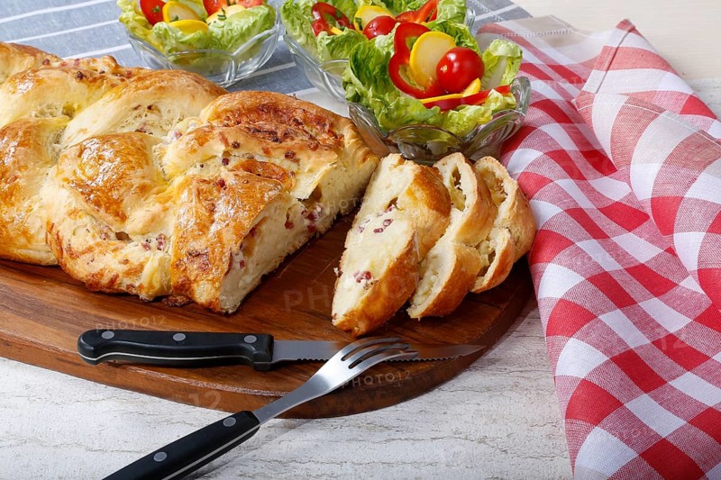 Swabian cuisine, hearty yeast plait with smoked meat, salty wreath bread, yeast yeast dough pastry, arranged on wooden board, baked, grandmother's kitchen, regional, home cooking, typical Swabian reinterpreted, traditional cuisine reinterpreted, salad in the back, small bowl, food photography, studio, Germany, Europe