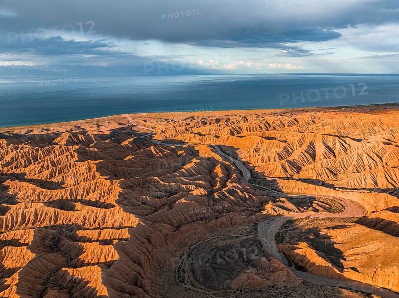 Riverbed runs through a landscape of eroded hills, badlands at sunset, Issyk Kul Lake in the background, aerial view, Canyon of the Forgotten Rivers, Issyk Kul, Kyrgyzstan, Asia