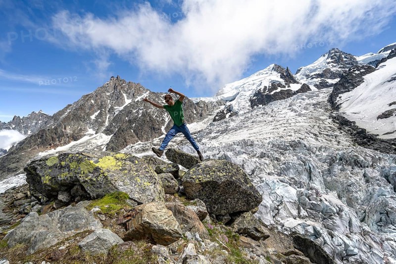 Mountaineer jumping from rock to rock, high alpine glaciated mountain landscape, La Jonction, Glacier des Bossons meets Glacier de Taconnaz, summit of Aiguille du Midi, Mont Maudit and Mont Blanc, Haute-Savoie, France, Europe