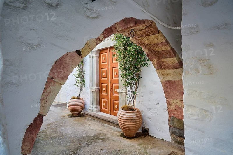 A historic stone Tor tor with plant pots and arches on a Greek island leading into a quiet courtyard, Skala, Patmos, Dodecanese, Greek Islands, Greece, Europe