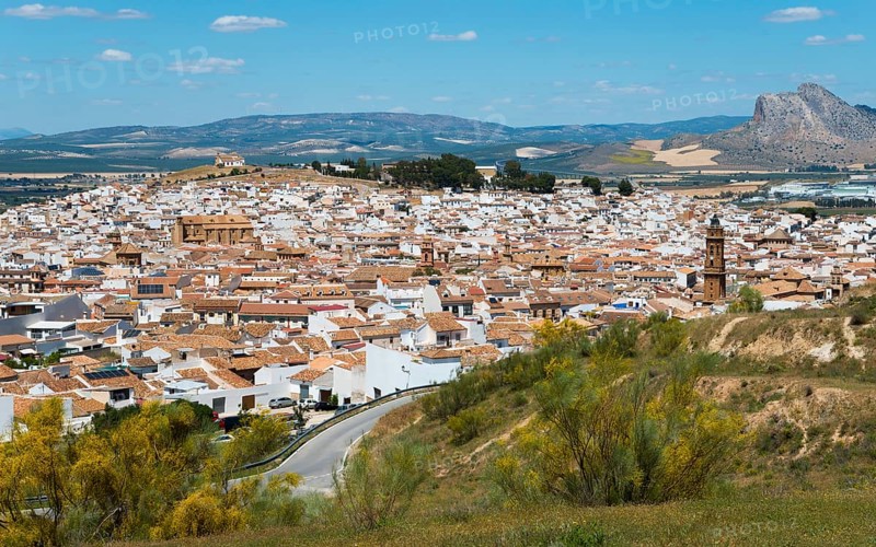 Spanish town with white buildings on a hill against a mountain backdrop under a blue sky, Antequera, Malaga, Andalusia, Spain, Europe
