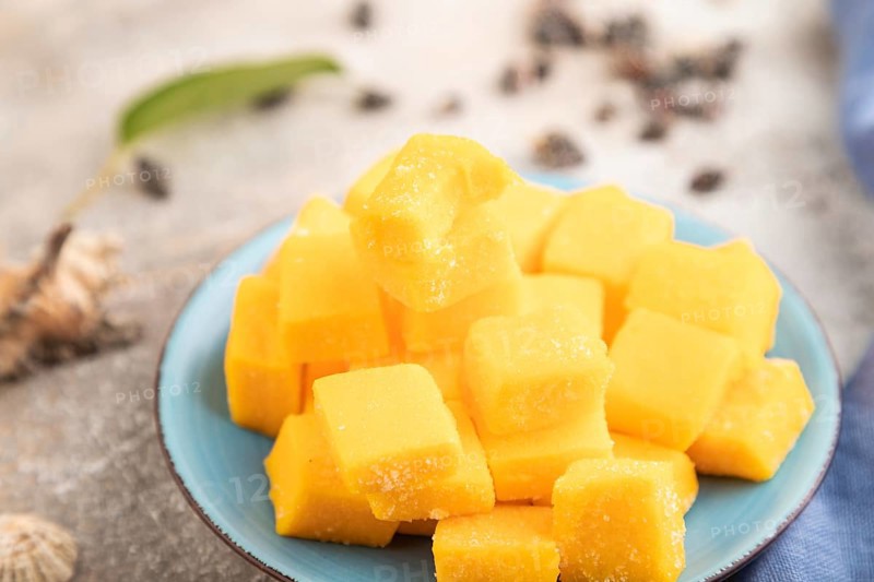 Dried and candied mango cubes on blue plate on brown concrete background and linen textile. Side view, close up, selective focus, vegan, vegetarian food concept