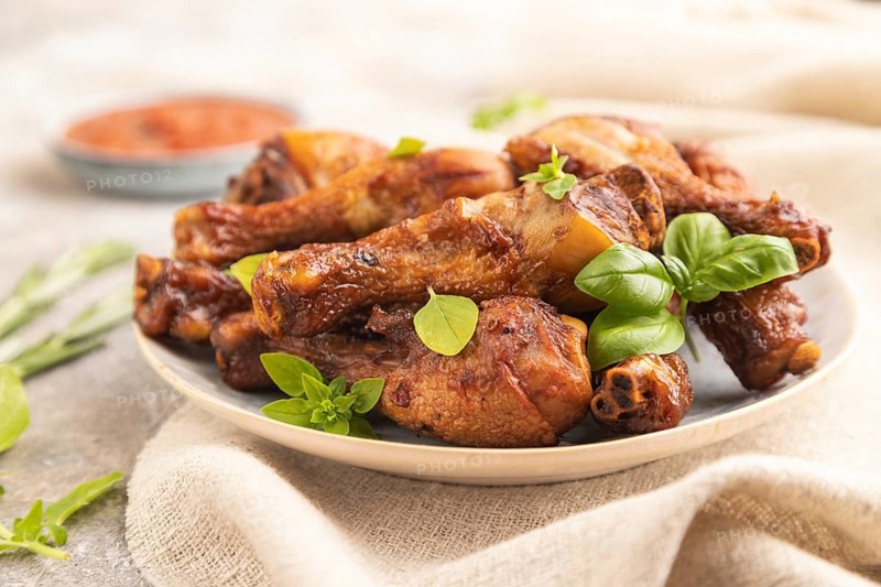 Smoked chicken legs with herbs and spices on a ceramic plate with linen textile on a brown concrete background. Side view, close up, selective focus