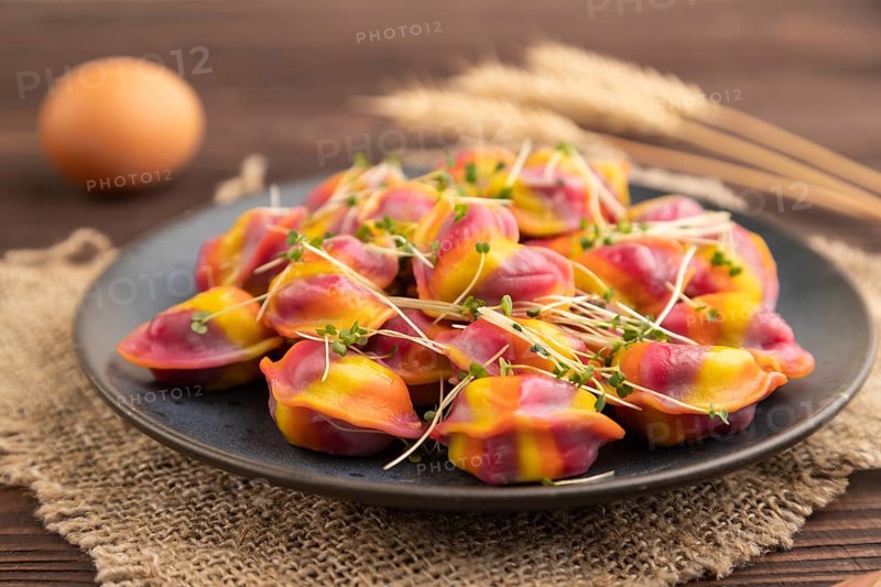 Rainbow colored dumplings with pepper, herbs, microgreen on brown wooden background and linen textile. Side view, close up, selective focus