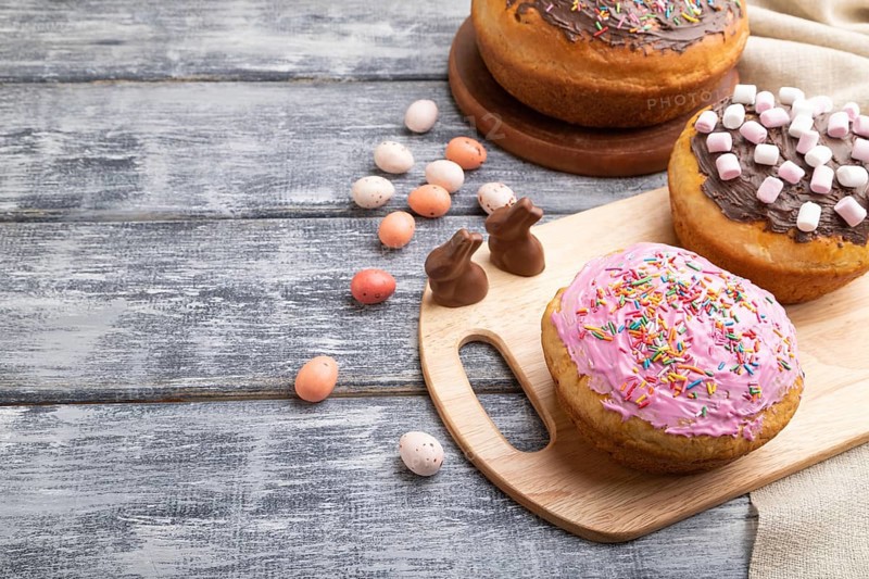 Homemade glazed and decorated easter pies with chocolate eggs and rabbits on a gray wooden background and linen textile. Side view, copy space