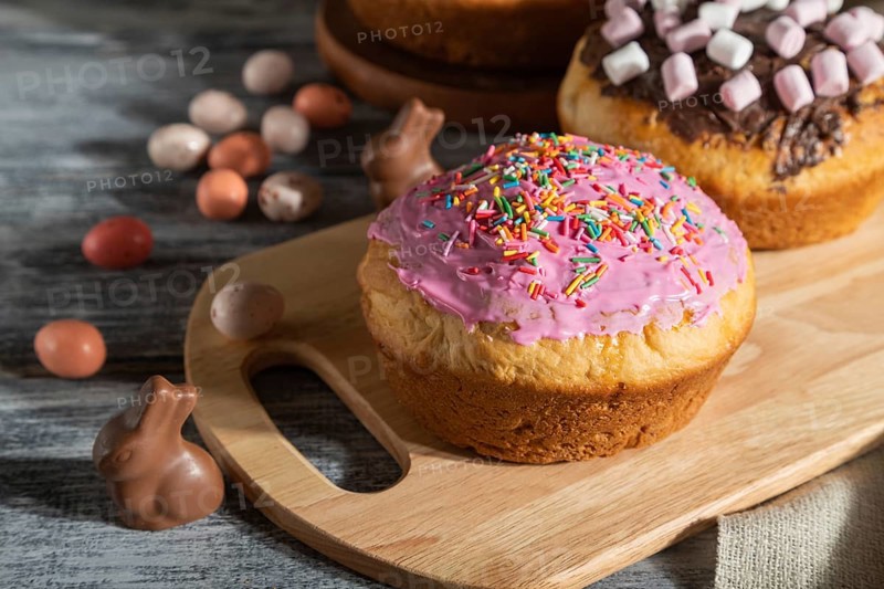 Homemade glazed and decorated easter pies with chocolate eggs and rabbits on a gray wooden background and linen textile. Hard light, contrast, Side view, close up
