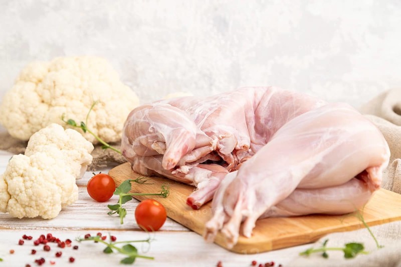 Whole raw rabbit with cauliflower, tomatoes and spices on a white wooden background and linen textile. Side view, close up, selective focus