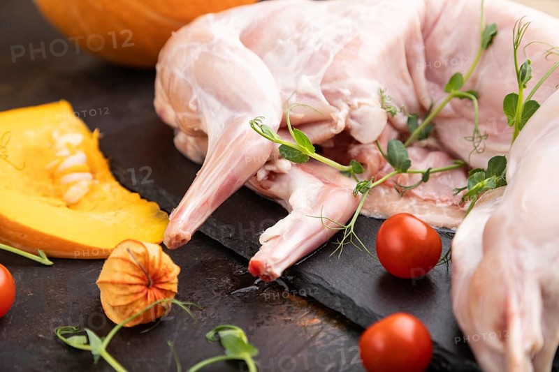 Whole raw rabbit with pumpkin, tomatoes, pea sprouts on a black concrete background and linen textile. Side view, close up, selective focus